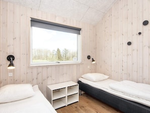 A room with two beds, a window, and a white shelf unit.