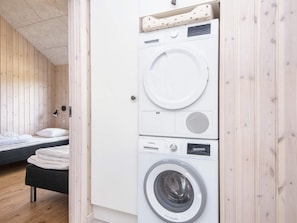 A compact room with a bed, a washing machine, and a small table.