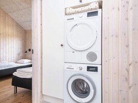 Habitación compacta con cama, lavadora y una pequeña mesa.