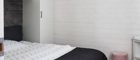 A bedroom with a bed, a wardrobe, a bedside table, and a pink ottoman.