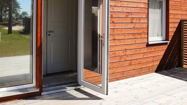 A wooden cabin with a sliding glass door leading to an outdoor deck. - 6 Person Holiday Home in Saffle (Saffle)