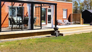 A modern house with a glass-enclosed patio, outdoor seating, and a barbecue area. - 6 Person Holiday Home in Saffle (Saffle)