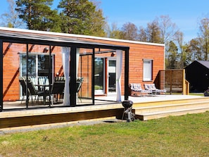 A modern house with a glass-enclosed patio, outdoor seating, and a barbecue area. - 6 Person Holiday Home in Saffle (Saffle)