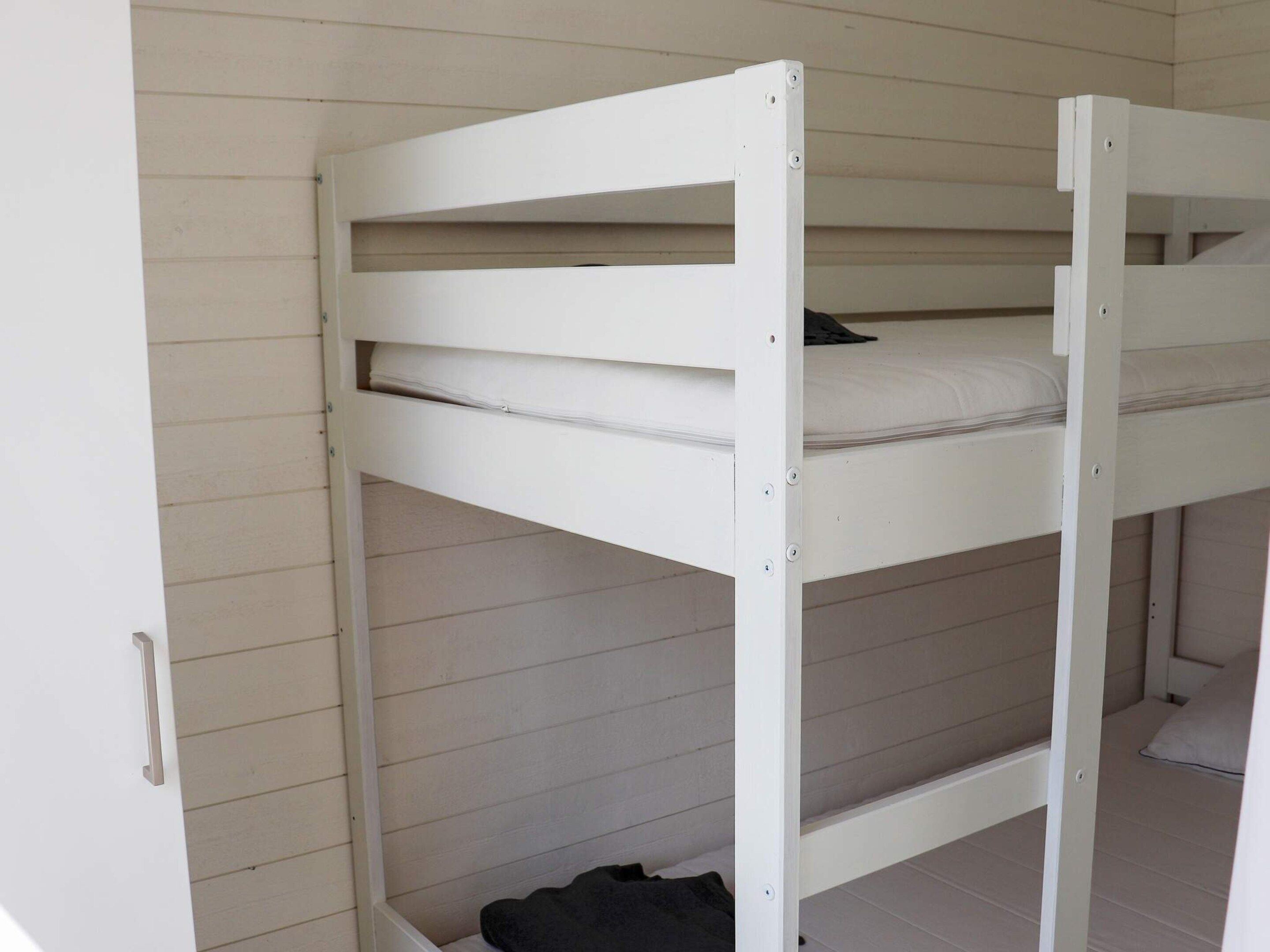 A bunk bed with a mattress and a pillow, a metal handle, and a white wall with horizontal lines.