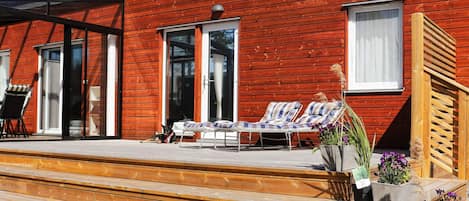 A wooden house with a covered patio, two lounge chairs, and a dog.