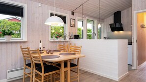A modern kitchen with wooden cabinets, a dining area with a wooden table and chairs, and a view of greenery outside. - 4 Person Holiday Home in Hejls (Hejls)