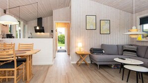 A modern interior with a wooden floor, a dining area with wooden chairs, a sofa, and a small table with a lamp. - 4 Person Holiday Home in Hejls (Hejls)