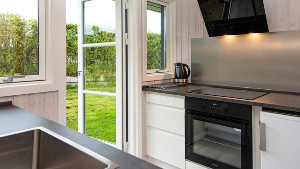 A modern kitchen with a stainless steel range hood, a built-in oven, and a window overlooking a garden. - 4 Person Holiday Home in Hejls (Hejls)