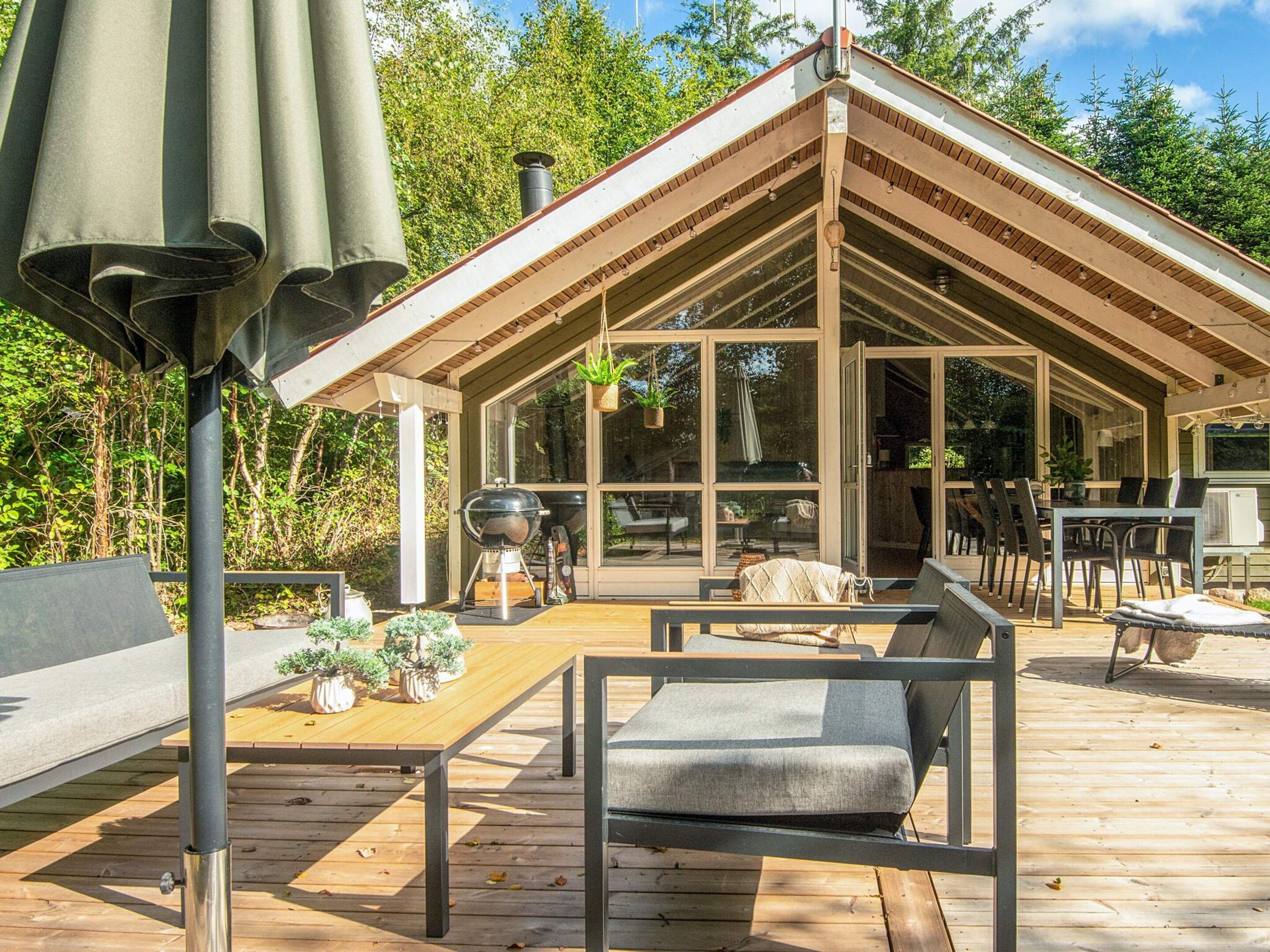 A modern outdoor deck with a wooden table, chairs, and a grill.