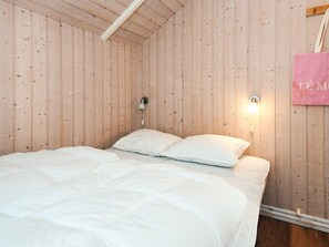 Une pièce aux murs en bois, un lit avec une literie blanche et deux appliques murales.