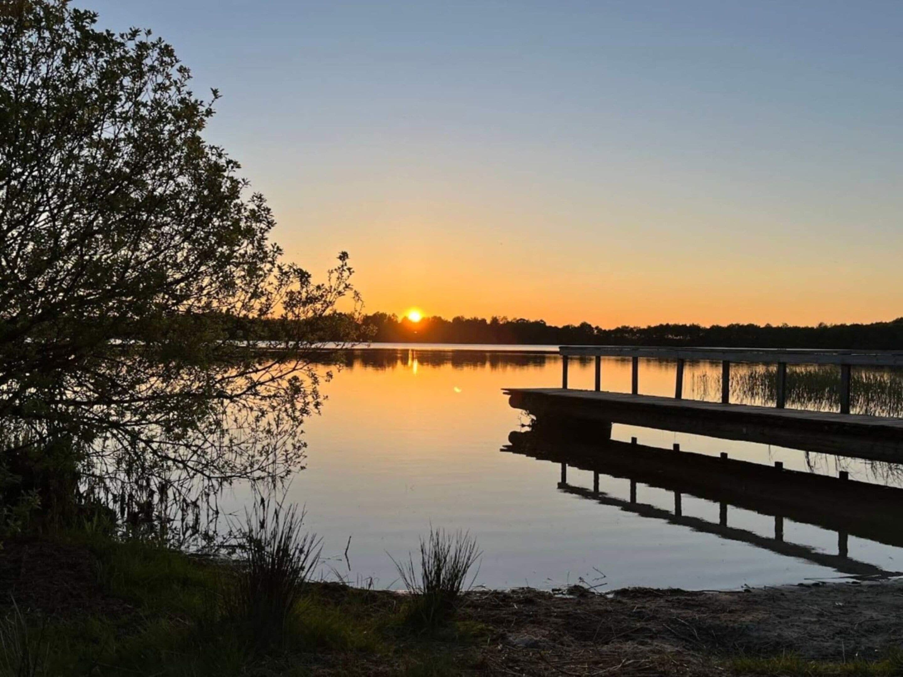 A calm lake at sunset with a dock extending into the water.