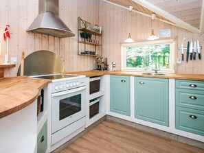 A kitchen with wooden walls, a stove, cabinets, and a window with a view of greenery.