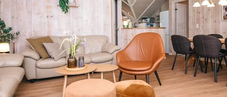 A modern interior with a sofa, armchair, ottoman, dining table, chairs, and a kitchen in the background.