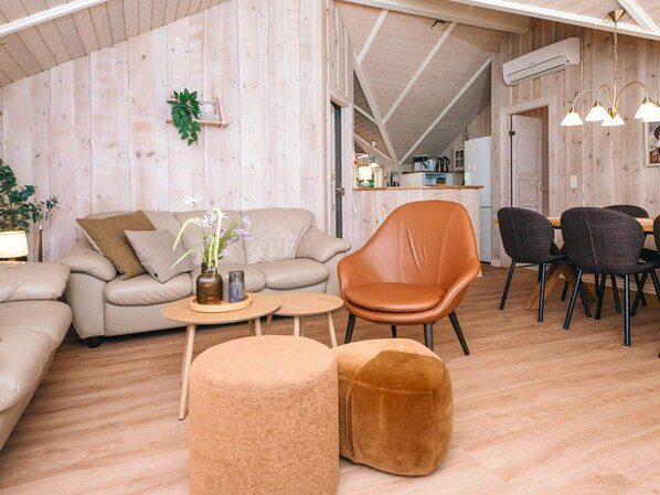 A modern interior with a sofa, armchair, ottoman, dining table, chairs, and a kitchen in the background.