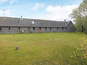A large, single-story building with a corrugated metal roof, multiple windows with red frames, and a grassy yard in front. - 12 Person Holiday Home in Thisted (Frøstrup)