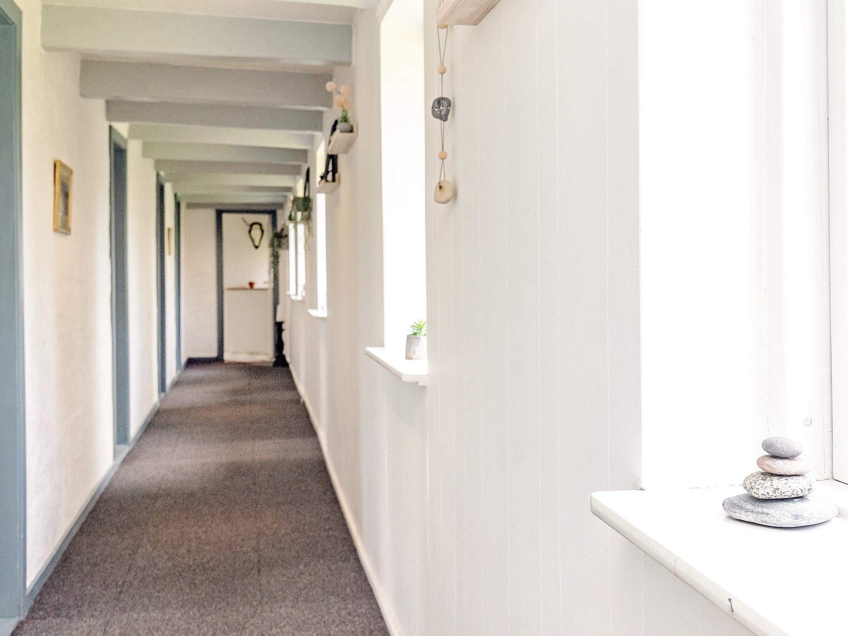 A corridor with a carpeted floor, white walls, and a shelf with decorative items.