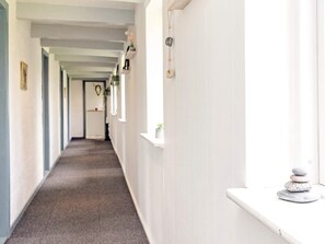 A corridor with a carpeted floor, white walls, and a shelf with decorative items.
