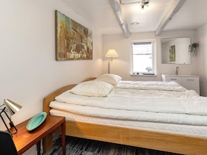 A bedroom with a bed, a bedside table, a lamp, a window, a mirror, and a painting on the wall.