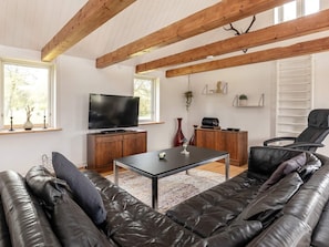 A modern living room with a leather sofa, a flat-screen TV, wooden beams, and a window with a view.