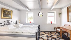 Un dormitorio con cama, dos ventanas, un espejo, una mesa de madera y una silla.