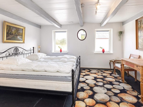 A bedroom with a bed, two windows, a mirror, a wooden table, and a chair.