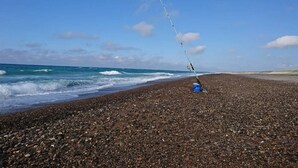 Una caña de pescar en una playa pedregosa con el océano al fondo.
