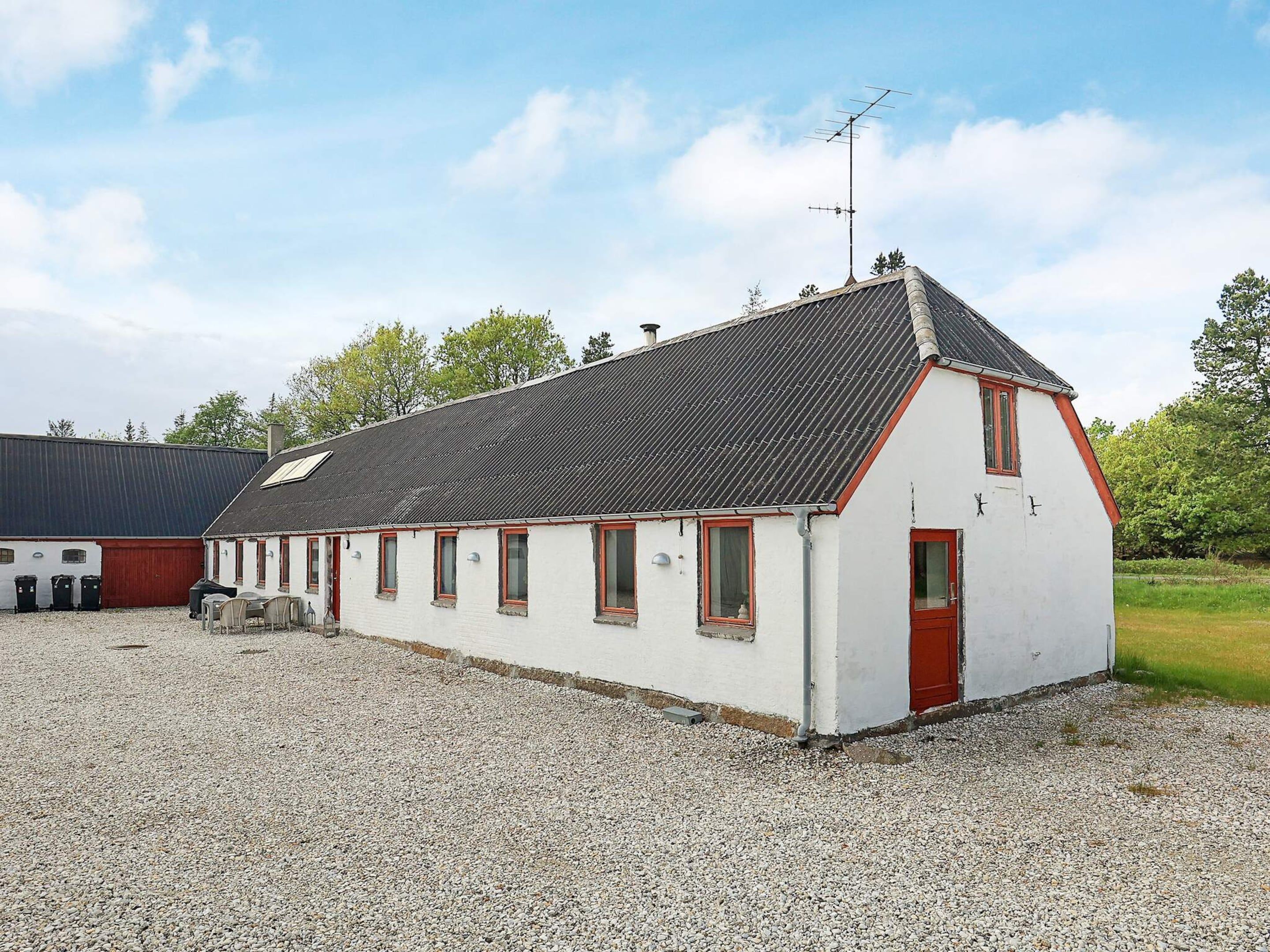 A white building with a red door and windows, a gravel driveway, and a metal roof.