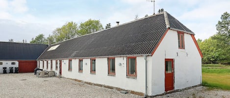 A white building with a red door and windows, a gravel driveway, and a metal roof.