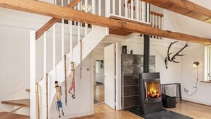 Una escalera con barandillas blancas y vigas de madera, una chimenea con repisa negra, y un cráneo de ciervo montado en la pared.