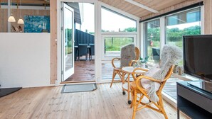 A modern interior with a wooden ceiling, a television, wicker chairs, and a glass door leading outside. - 8 Person Holiday Home in Lokken (Lokken)