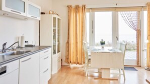 A modern kitchen with a built-in dishwasher, a dining area with a table and chairs, and a large window with curtains. - 4 Star Holiday Home in Allinge (Allinge)