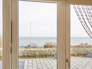 A view through a glass door to a patio area with a paved walkway, a metal railing, and a view of the sea.
