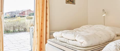 Een slaapkamer met een bed, een raam met gordijnen, een wandlamp en een schilderij.