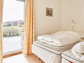 A bedroom with a bed, a window with curtains, a wall-mounted lamp, and a painting.