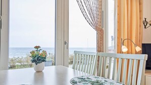 A dining area with a view of the sea, a white table, two chairs, a potted plant, and a table runner. - 4 Star Holiday Home in Allinge (Allinge)