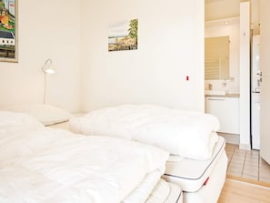 Habitación de hotel con dos camas, una mesita de noche, una lámpara de pared, un pequeño cuadro y vistas al área de la cocina contigua.