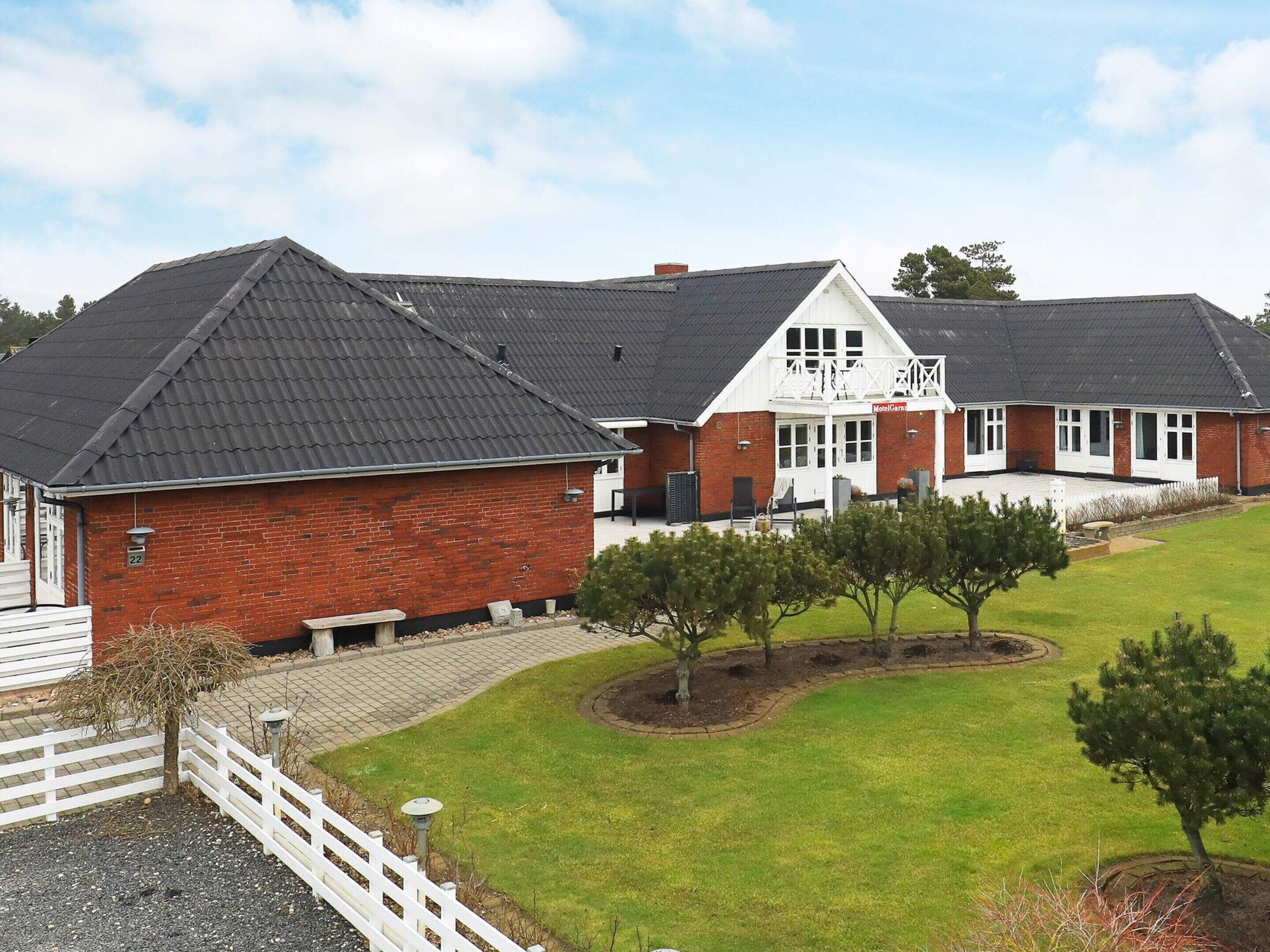 A two-story brick building with a balcony, a covered patio, and a fenced yard with trees.