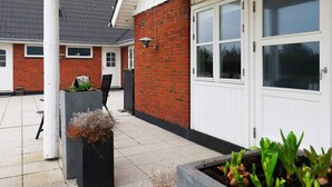 A residential building with a red brick exterior, white doors, and a tiled patio area with planters. - 6 Person Holiday Home in Blavand (Blavand)