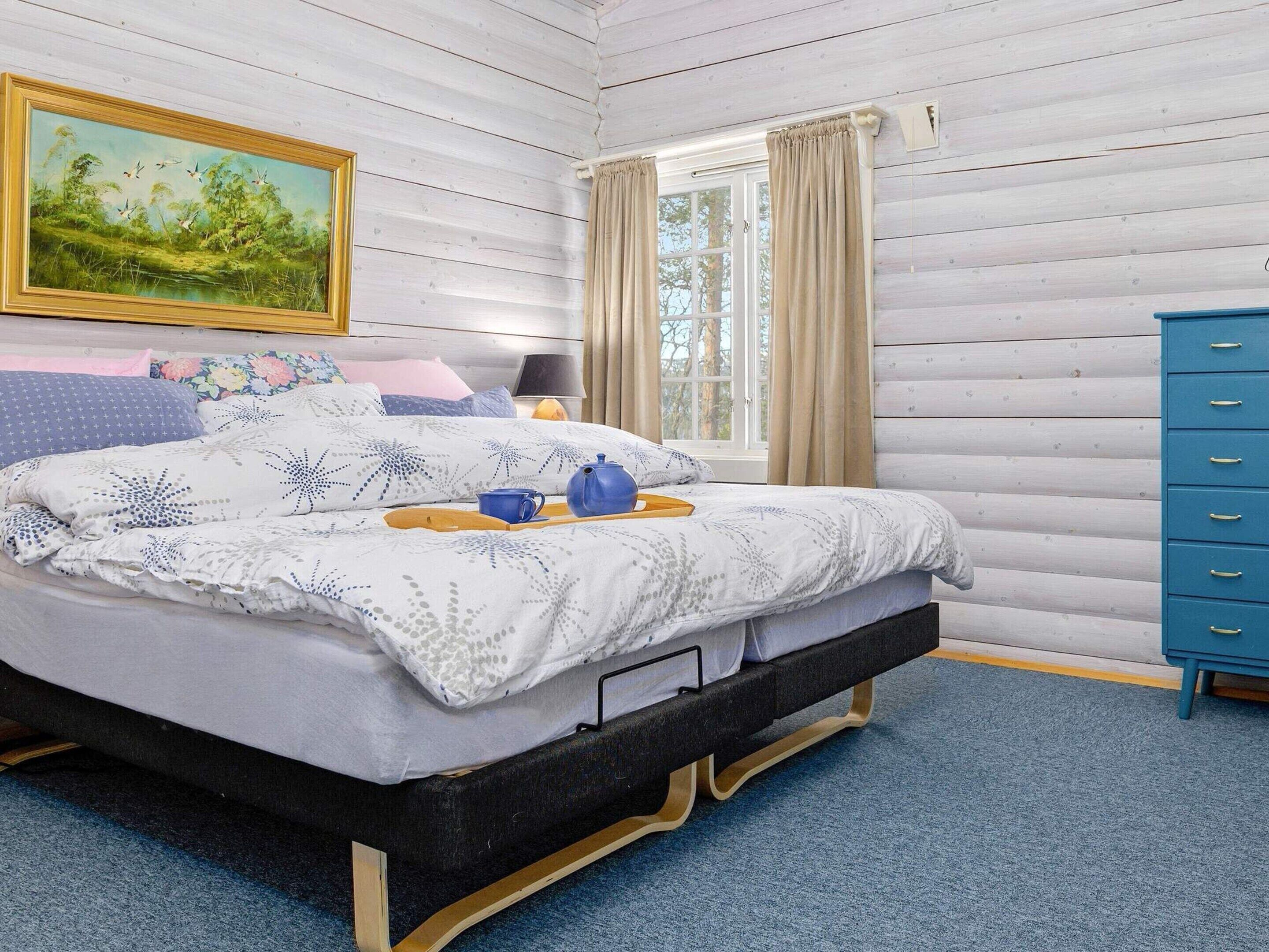 Un dormitorio con cama, un cuadro, una ventana con cortinas y un aparador azul.
