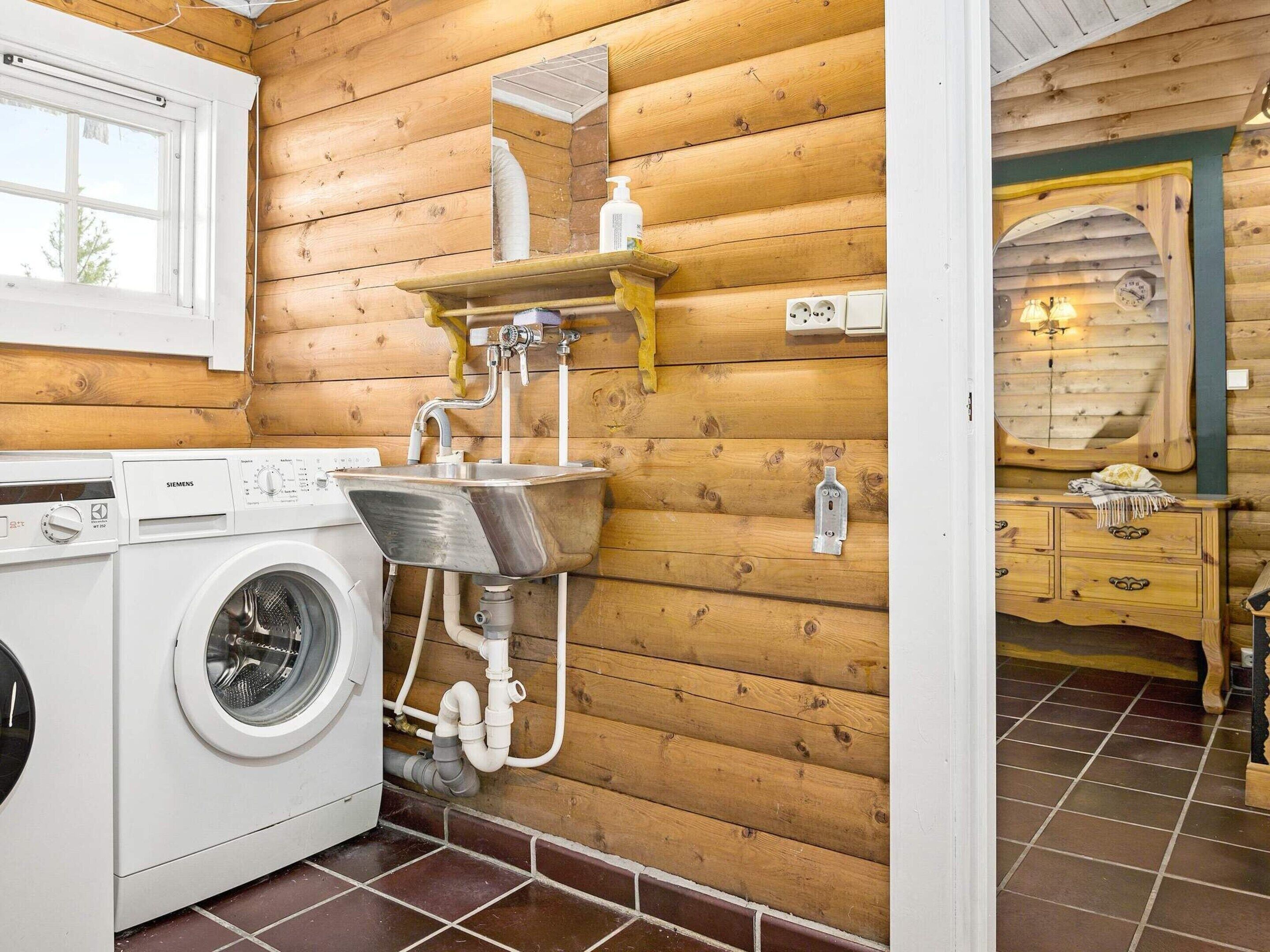 A compact, wood-paneled bathroom with a washing machine, a sink, and a mirror.