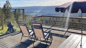 Een houten terras met twee stoelen en een parasol, met uitzicht op een bergachtig landschap.