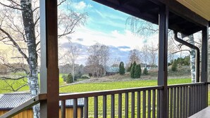 A covered outdoor area with a wooden deck and a view of a green field and trees. - 4 Person Holiday Home in Vittbolandet (Vikbolandet)