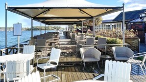 A covered outdoor seating area with tables and chairs, overlooking a body of water. - 4 Person Holiday Home in Vittbolandet (Vikbolandet)