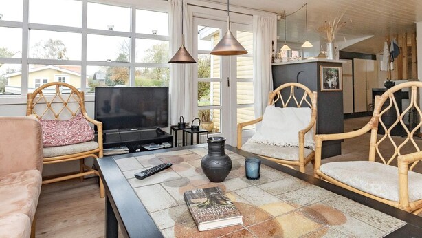 A living room with a television, two wicker chairs, a sofa, a coffee table, and a large window offering a view of the outside. - 6 Person Holiday Home in Haarby (Haarby)
