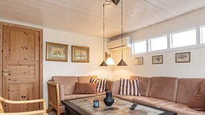 A cozy living room with a wooden door, a beige sofa, a glass coffee table, and a wicker chair. - 6 Person Holiday Home in Haarby (Haarby)