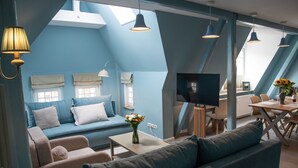 Ein stilvolles Loft-Zimmer in Blau mit einer Couch, einem Esstisch und einem Fernseher.