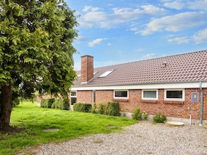 A two-story brick house with a tiled roof, a chimney, and a small garden with a tree and shrubs.