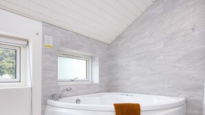 A modern bathroom with a freestanding bathtub, a window, and tiled walls.