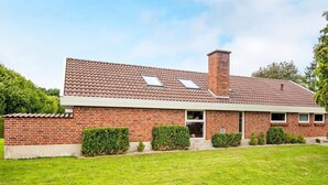 A two-story brick house with a tiled roof, a chimney, and a well-maintained lawn.