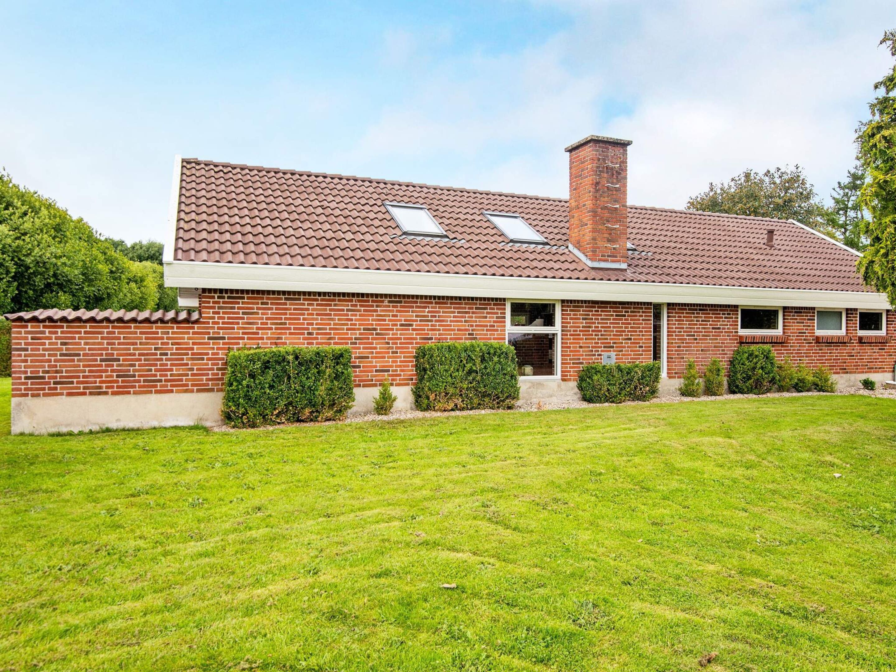 A two-story brick house with a tiled roof, a chimney, and a well-maintained lawn.
